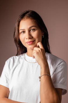 Studio portrait of a young woman in a white t-shirt with a thoughtful expression, smiling.